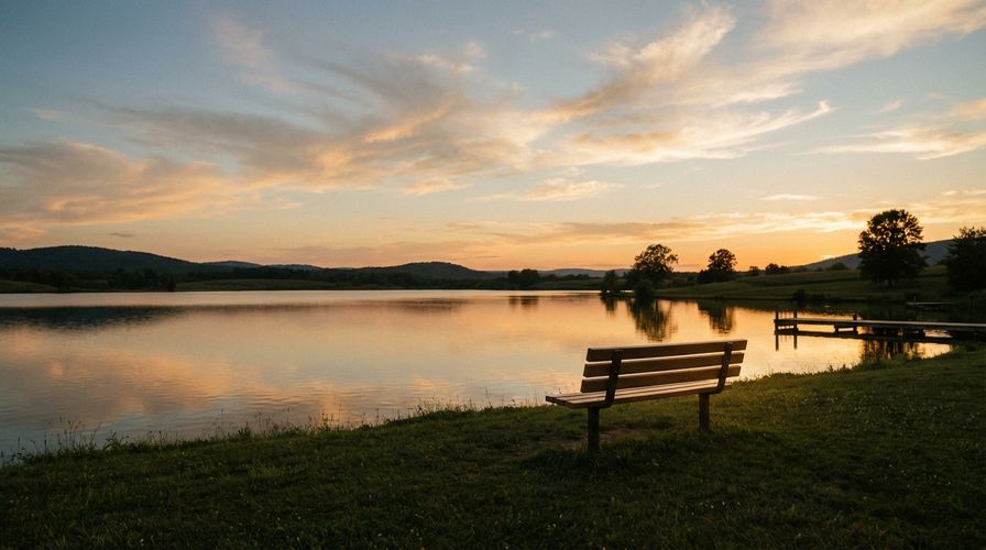 Serene sunset over a calm lake with a single empty bench, peaceful and contemplative atmosphere